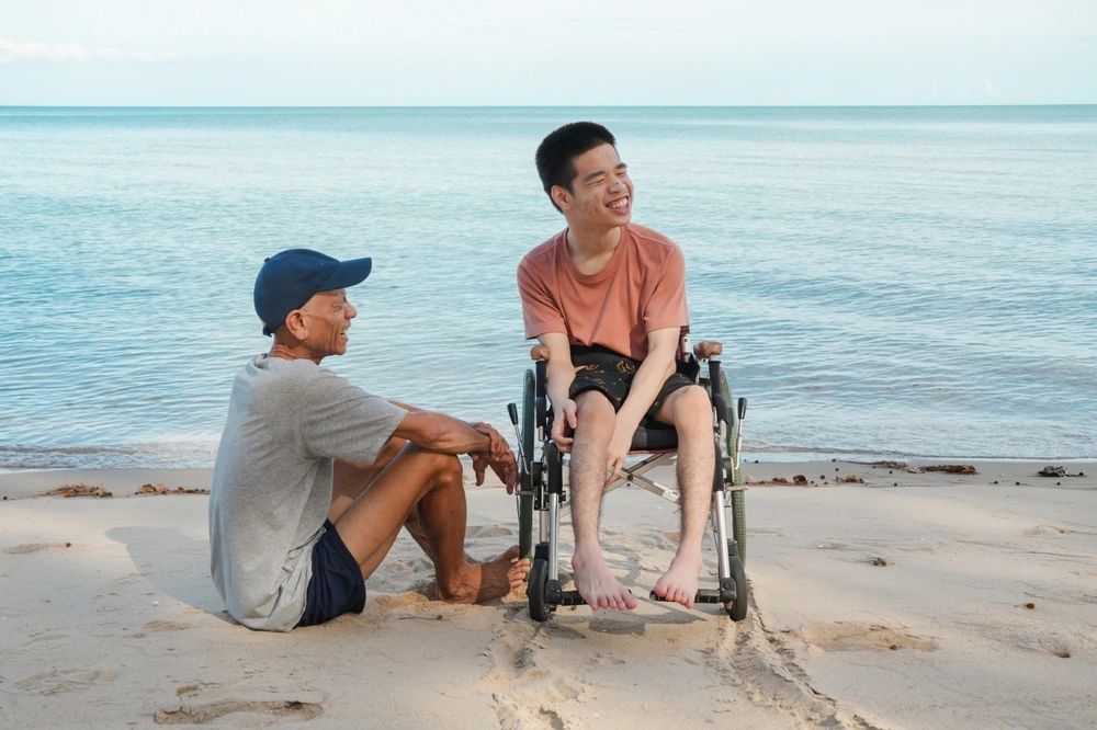 disabled young boy with care assistant, hanging out by the beach